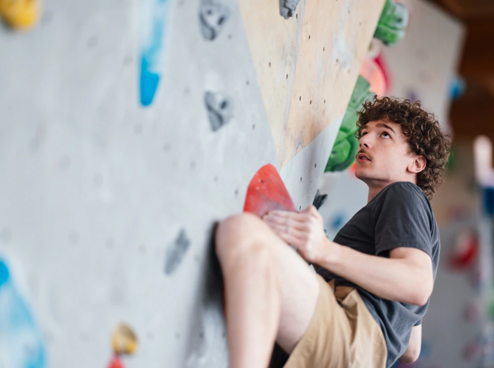 A focused young man practising bouldering on an indoor climbing wall with colourful holds.
